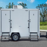 Side view of a white restroom trailer with men’s and women’s doors and metal steps.