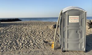 porta potty on beach with surf board propped against it.