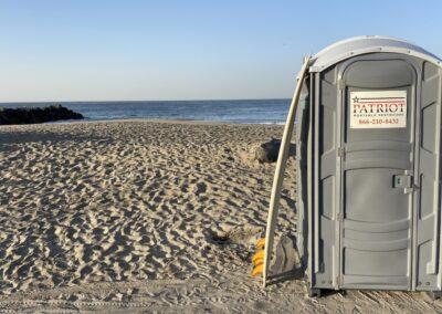 porta potty on beach with surf board propped against it.