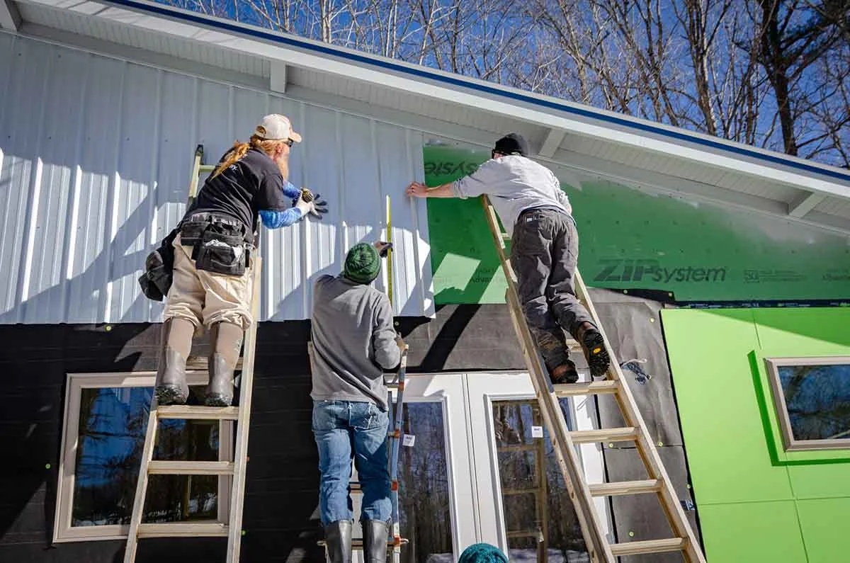 Construction workers on ladders siding a building
