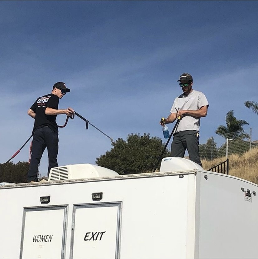 Two of our employees powerwashing the top of one of our large luxury restroom trailer rentals.