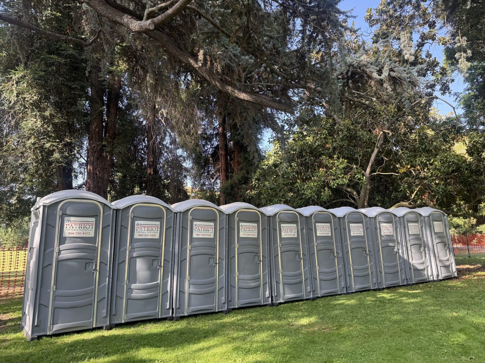 Row of Patriot portable toilets set up under trees at a festival