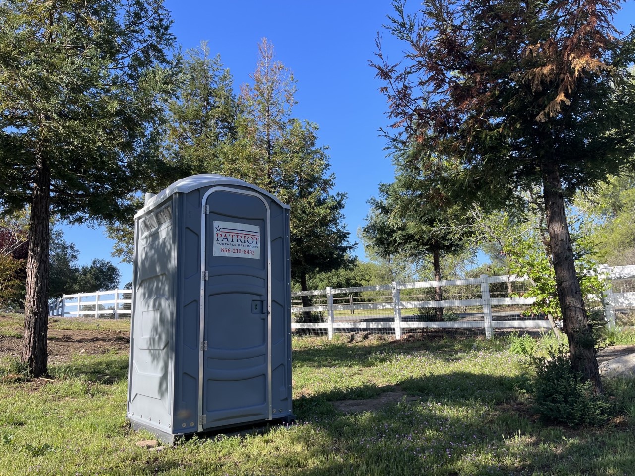 Patriot portable toilet on farmland beside a fence line