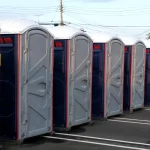 Multiple gray portable toilets arranged in a parking lot ready for rental and event use