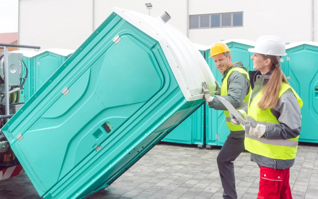 Workers delivering and setting up portable restroom units at a job site using professional equipment