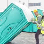 Workers delivering and setting up portable restroom units at a job site using professional equipment