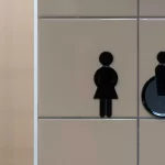 Restroom wall sign showing female and wheelchair accessibility icons on beige square tiles.