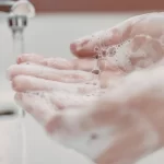 Soapy hands held under running water during handwashing in a bright, clean sink area indoors.