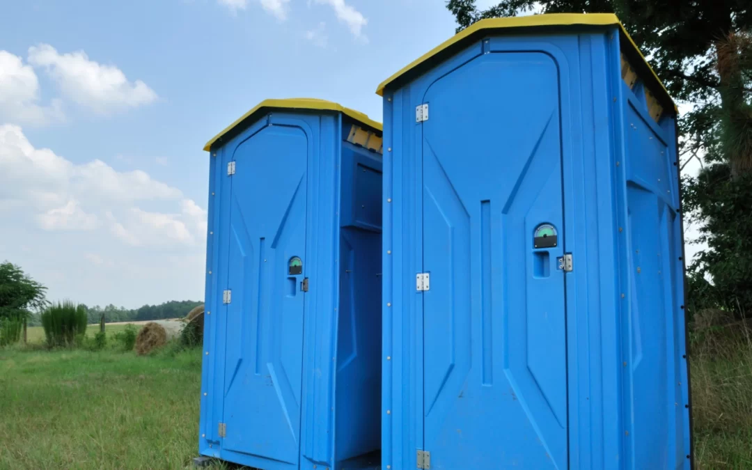 Blue portable restroom units with open gap between them in a rural field under scattered clouds