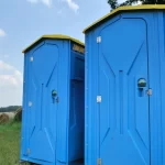Blue portable restroom units with open gap between them in a rural field under scattered clouds